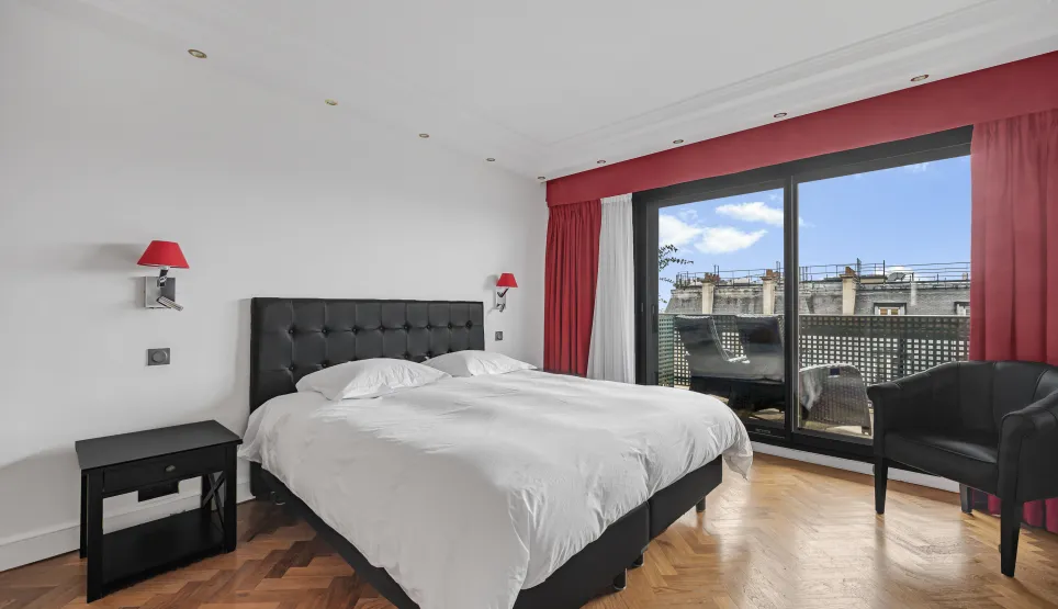 Chambre de luxe moderne avec lit king-size, parquet, balcon privé et vue ville. Design élégant et lumineux pour un confort optimal.