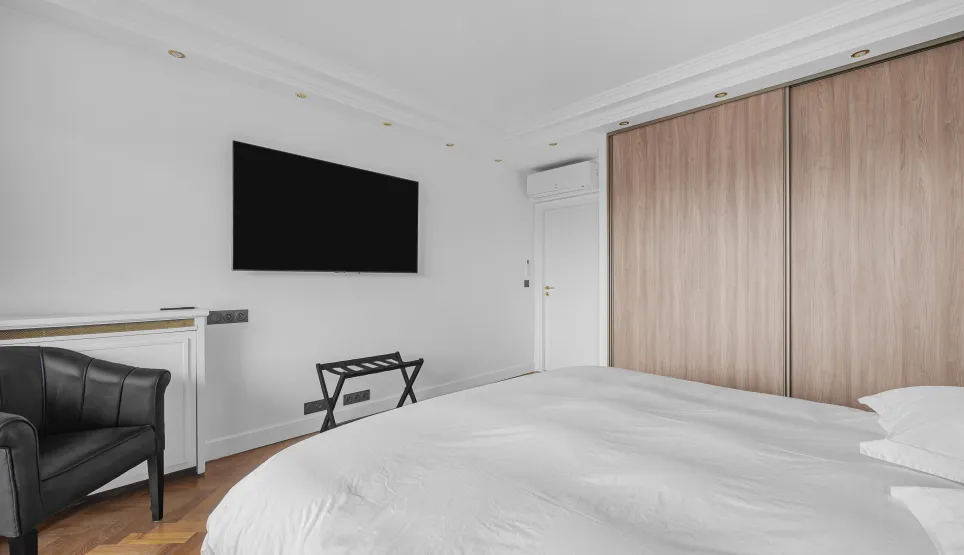 Chambre parentale moderne et élégante avec lit double, TV murale, dressing intégré bois, fauteuil design. Confort et luxe pour votre appartement.