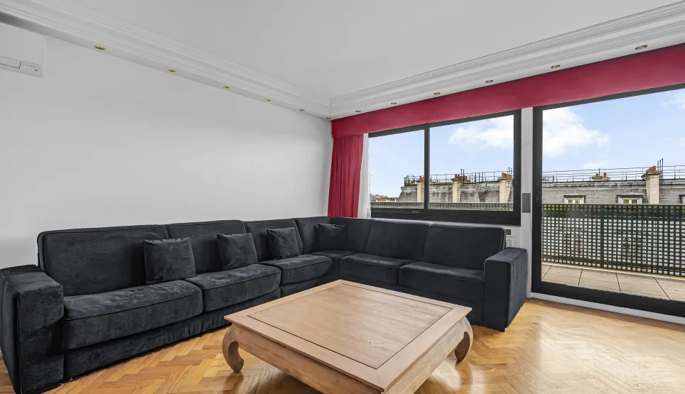 Salon moderne et lumineux d'un appartement de luxe. Grand canapé, parquet, vue sur les toits de Paris et balcon.