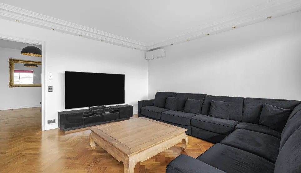 Salon de luxe moderne avec grand canapé d'angle, TV, parquet chevron. Confort et élégance pour votre intérieur.