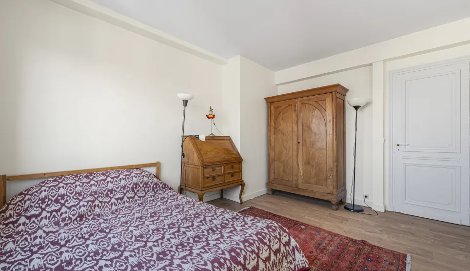 Chambre élégante avec mobilier ancien en bois massif : armoire, bureau secrétaire. Lit confortable, parquet, tapis oriental. Charme intemporel.