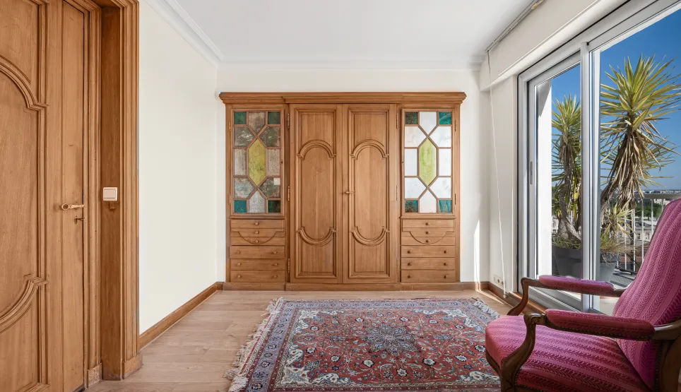 Élégant dressing en bois sur mesure avec vitraux, parquet et tapis oriental. Accès terrasse lumineuse. Ambiance chic et chaleureuse.