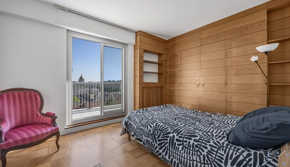 Chambre élégante avec boiseries, parquet, et balcon offrant une vue imprenable sur le dôme de la ville. Luxe et sérénité au cœur de l'appartement.