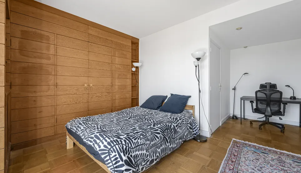 Chambre élégante avec grand rangement intégré en bois, parquet, et espace bureau discret. Confort et style pour un intérieur de luxe.