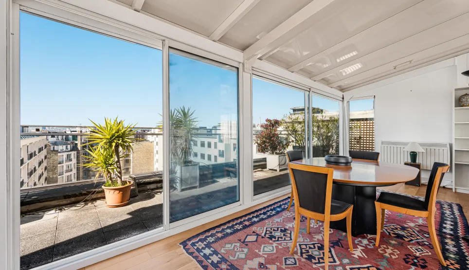 Salle à manger lumineuse avec vue panoramique sur la ville et accès terrasse. Un espace de vie urbain élégant et ensoleillé.