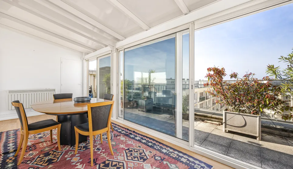 Lumineuse véranda/solarium avec salle à manger, accès direct à une terrasse privée offrant une vue dégagée sur la ville. Idéal pour un penthouse de luxe.