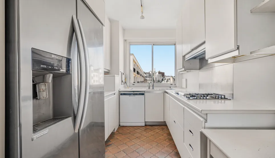 Cuisine contemporaine blanche, entièrement équipée, avec réfrigérateur américain, plaque de cuisson gaz et belle vue urbaine. Luxe et fonctionnalité.