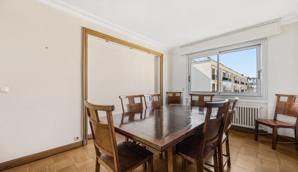 Salle à manger spacieuse et lumineuse avec parquet, grande table en bois massif et vue urbaine. Idéal pour un appartement de luxe.