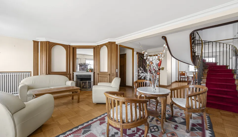 Salon de luxe élégant avec cheminée, boiseries, parquet et majestueux escalier en colimaçon. Propriété spacieuse.