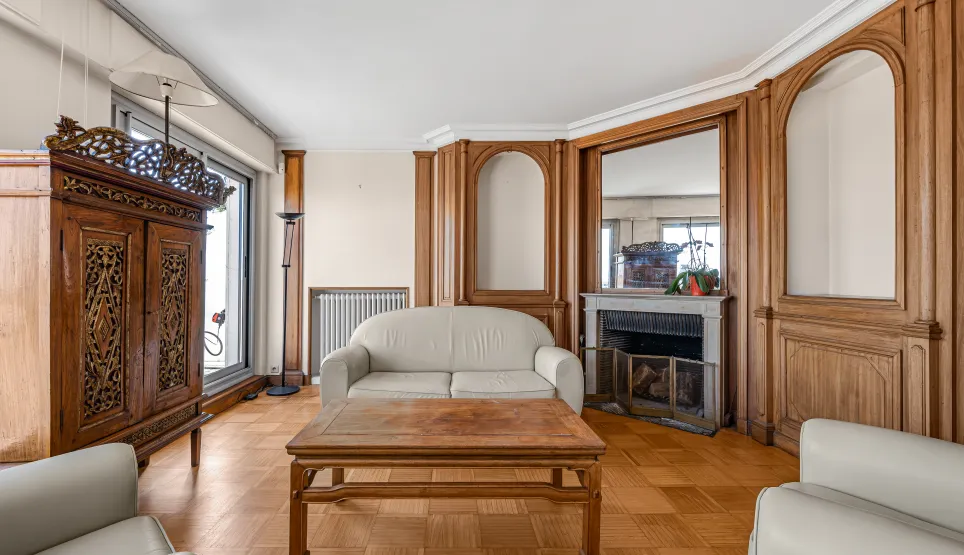 Salon de luxe avec boiseries murales, parquet, cheminée et mobilier classique. Une élégance intemporelle pour un appartement d'exception.
