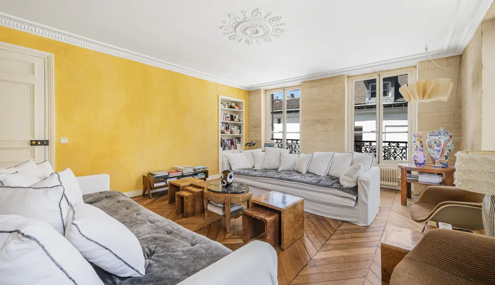 Salon de luxe lumineux avec mur jaune texturé, parquet, moulures et canapés blancs. Élégance parisienne.
