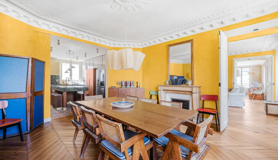 Élégante salle à manger parisienne aux murs jaunes, parquet chevron, cheminée. Appartement de luxe rénové, alliant charme ancien et design moderne.
