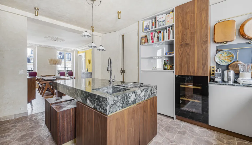 Cuisine de luxe avec îlot central en marbre et bois, design moderne et élégant. Espace ouvert sur salle à manger. Appartement haussmannien.