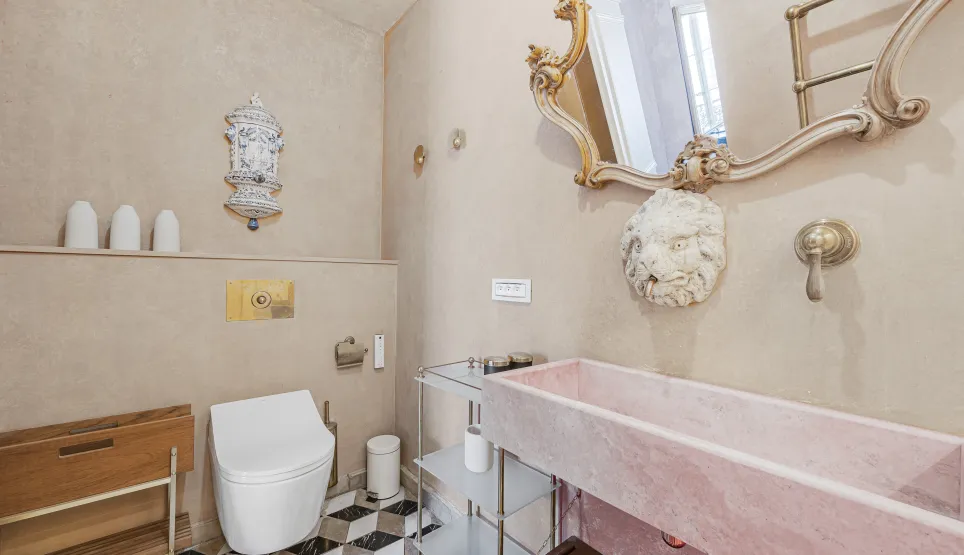 Salle de bain luxe avec lavabo marbre rose, miroir doré, toilettes design et carrelage géométrique. Ambiance élégante et raffinée.