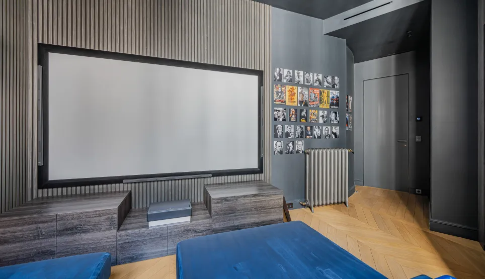 Salle de cinéma privée de luxe au design moderne. Écran géant, boiseries élégantes, parquet chevrons. Expérience immersive haut de gamme.