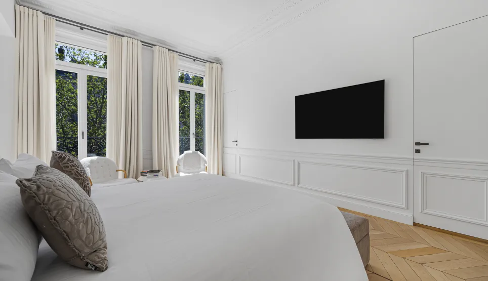Chambre de luxe moderne, lumineuse. Grandes fenêtres, parquet chevron, TV murale. Design élégant et épuré pour un espace serein et confortable.