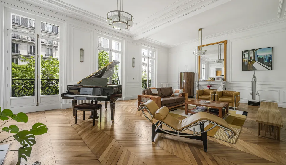 Luxe parisien: salon élégant avec grand piano, parquet chevrons, moulures et vue verdoyante. Design intemporel.