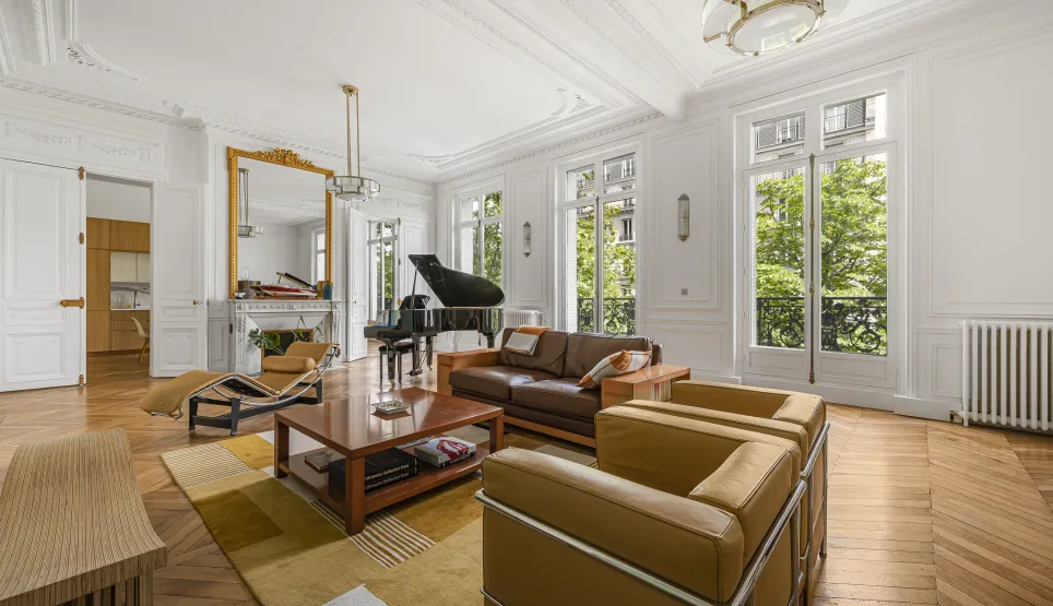 Salon Haussmannien de luxe à Paris: piano, parquet, moulures, cheminée, vue verdoyante. Élégance et lumière.