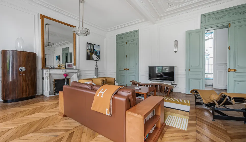 Appartement Haussmannien luxueux, salon lumineux avec parquet chevron, moulures, cheminée et mobilier design Art Déco.