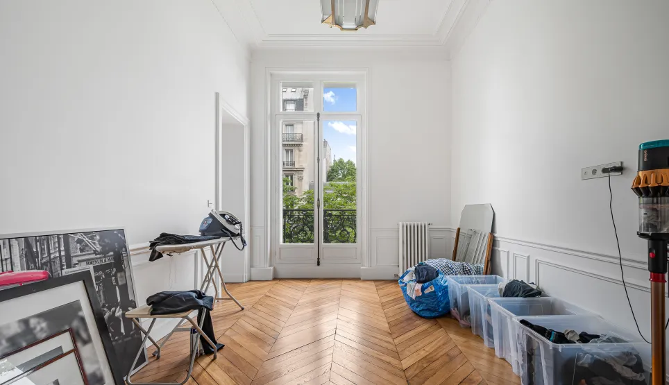Appartement haussmannien Paris. Pièce lumineuse, parquet chevrons, moulures, fenêtre balcon. Potentiel luxe, vue verdoyante.