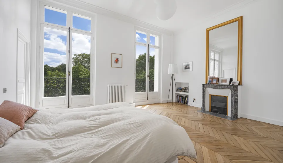 Chambre luxueuse et lumineuse avec vue imprenable sur la verdure. Parquet chevrons, cheminée et miroir doré. Élégance et confort.