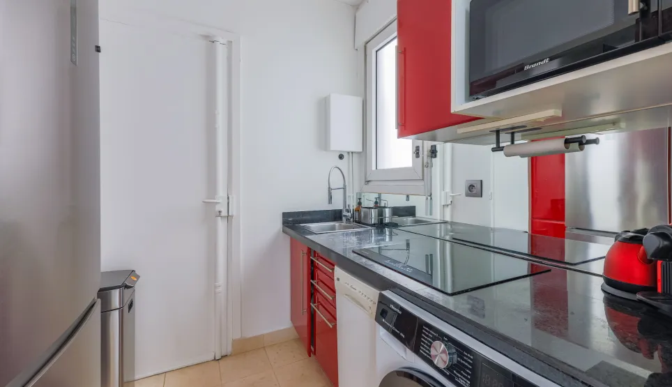 Cuisine moderne et élégante, entièrement équipée (lave-linge, micro-ondes), design contemporain rouge et noir. Idéal pour appartement de luxe.