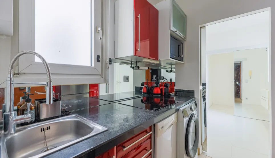 Cuisine design compacte, placards rouges brillants, plan de travail granit. Électroménager intégré. Parfait pour appartement urbain moderne.