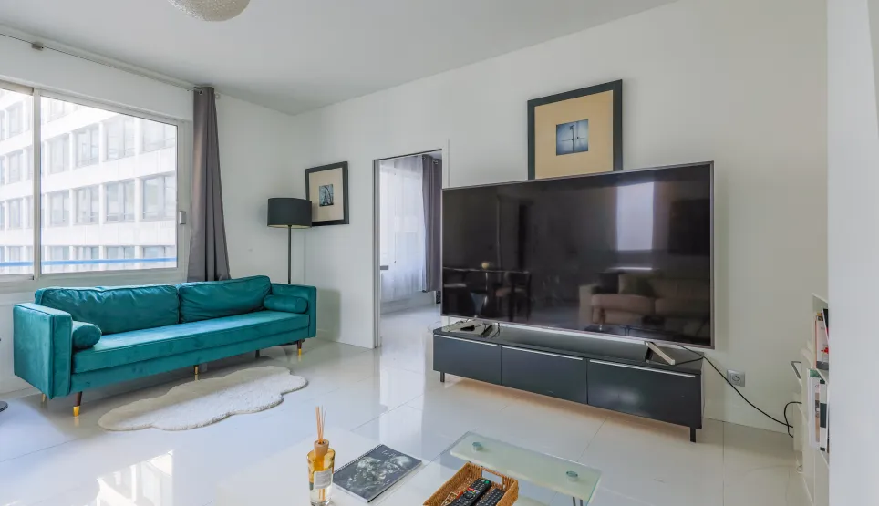 Salon moderne et lumineux avec canapé velours bleu canard, grand écran TV, design épuré. Idéal pour un appartement de luxe urbain. Confort et style.