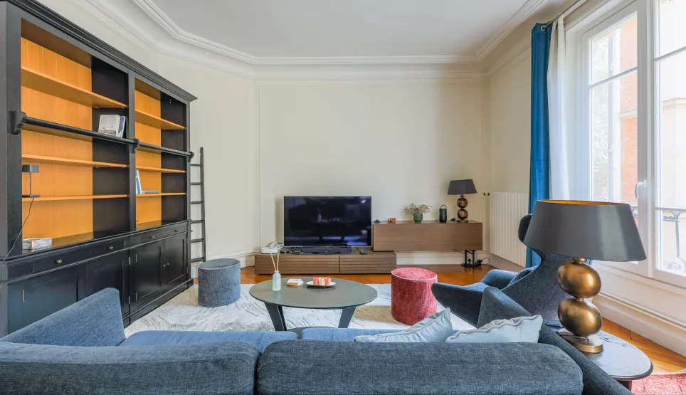 Salon parisien élégant et lumineux avec bibliothèque intégrée, canapé design et TV. Idéal pour un appartement de luxe.