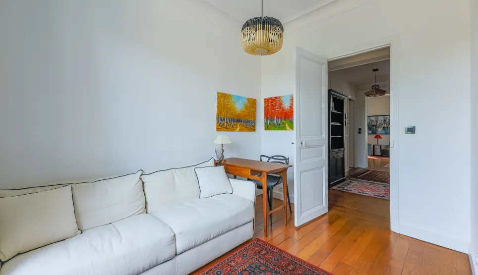 Espace de vie lumineux et raffiné: canapé design, bureau élégant, parquet chaleureux, œuvres d'art vibrantes. Idéal pour un intérieur de prestige.