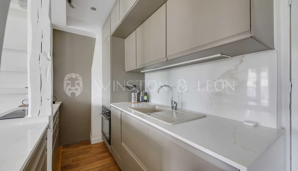 Cuisine moderne et élégante avec meubles gris clair, plan de travail et crédence en marbre. Design luxueux pour appartement parisien.