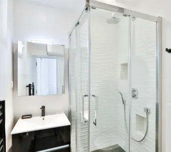 Salle de bain moderne et lumineuse avec douche à l'italienne, vasque design et miroir. Luxe épuré pour appartement contemporain.