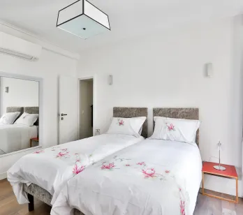 Élégante chambre moderne avec lits jumeaux, climatisation, miroir et décoration florale. Confort et design pour votre propriété de luxe.