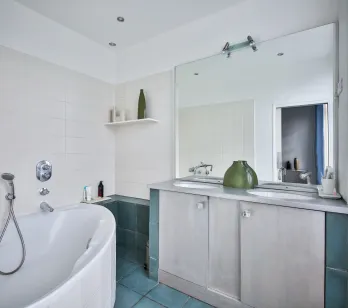 Salle de bain de luxe moderne: baignoire, double vasque, grand miroir, carrelage blanc/bleu. Design épuré, ambiance zen. Idéal propriété haut de gamme.