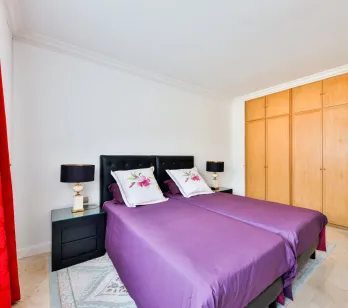 Chambre élégante avec lits jumeaux, literie violette, tables de chevet design et placards intégrés. Confort et style pour propriété de luxe.