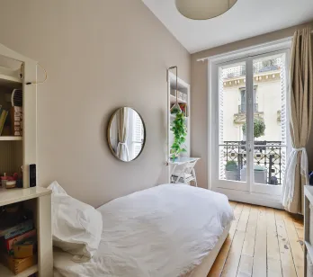 Chambre parisienne lumineuse avec balcon, parquet clair et vue dégagée. Lit simple, rangements intégrés. Idéal pour enfant ou bureau d'appoint. Charme et potentiel.