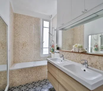 Salle de bain moderne et lumineuse avec double vasque, baignoire, carrelage élégant et miroir intégré. Design contemporain pour un confort optimal.