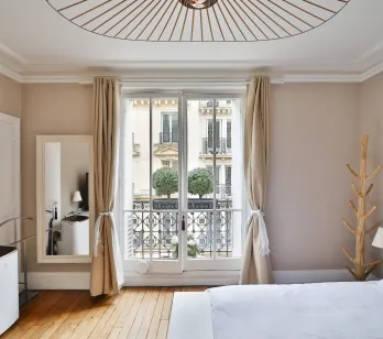 Chambre de luxe parisienne avec balcon, parquet, luminaire design. Élégance et vue urbaine pour un séjour raffiné.