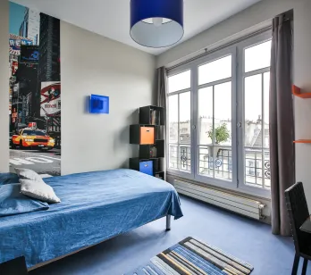 Chambre moderne et lumineuse d'un appartement de luxe. Lit confortable, vue ville, décoration urbaine chic avec fresque Times Square. Design contemporain.