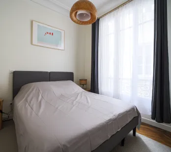 Chambre élégante et lumineuse avec lit double, décoration moderne et fenêtre offrant une belle lumière naturelle. Idéal pour un appartement de luxe.