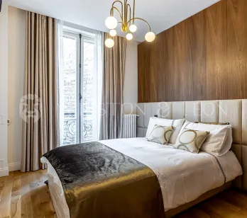 Chambre de luxe moderne avec boiseries murales, tête de lit rembourrée et lustre élégant. Confort et design contemporain pour un appartement parisien.
