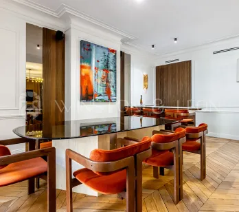 Intérieur de luxe moderne: salle à manger élégante avec table en verre, chaises orange velours, art contemporain et parquet. Design raffiné.