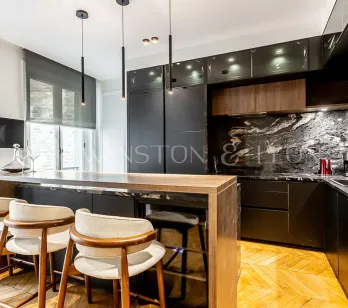 Cuisine luxe moderne avec îlot bois, marbre noir veiné, tabourets design et luminaires suspendus.