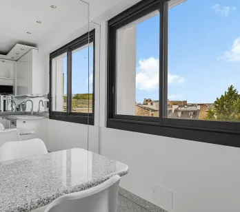 Cuisine moderne lumineuse, îlot en granit, vue urbaine. Design épuré pour un appartement de luxe contemporain.