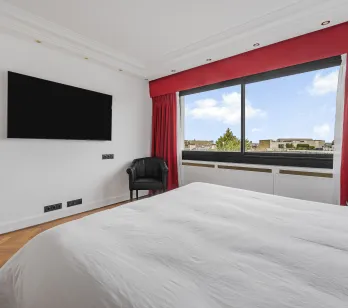 Suite parentale moderne et lumineuse avec vue citadine, TV, fauteuil et parquet. Le luxe et le confort d'un appartement haut de gamme.