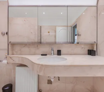 Salle de bain luxueuse en marbre clair, lavabo design et miroir. Ambiance raffinée pour une propriété d'exception.