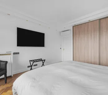 Chambre parentale moderne et élégante avec lit double, TV murale, dressing intégré bois, fauteuil design. Confort et luxe pour votre appartement.