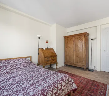 Chambre élégante avec mobilier ancien en bois massif : armoire, bureau secrétaire. Lit confortable, parquet, tapis oriental. Charme intemporel.