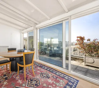 Lumineuse véranda/solarium avec salle à manger, accès direct à une terrasse privée offrant une vue dégagée sur la ville. Idéal pour un penthouse de luxe.