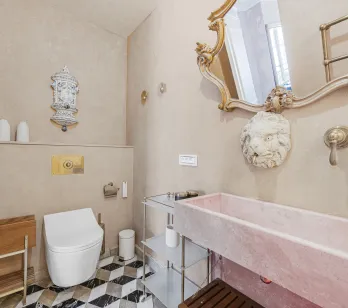 Salle de bain luxe avec lavabo marbre rose, miroir doré, toilettes design et carrelage géométrique. Ambiance élégante et raffinée.